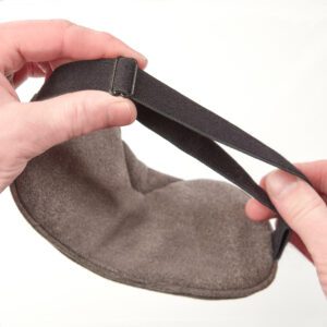 Slumbar eye mask against white background with a males hands showing how to adjust the strap for the perfect fit