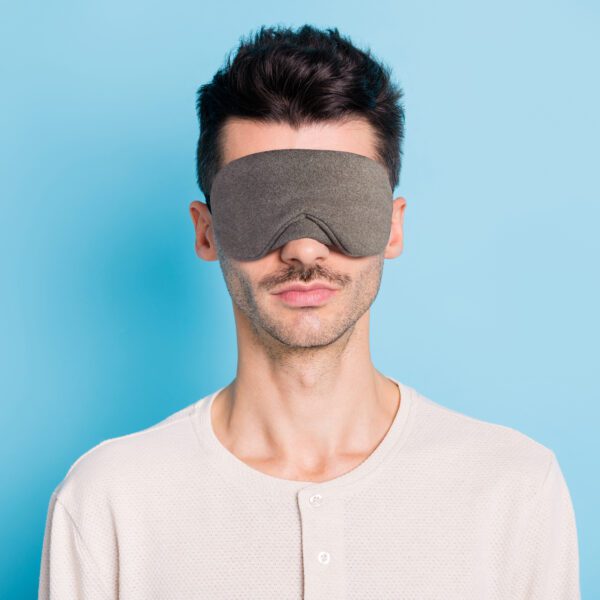 Portrait of nice calm brunet guy wearing sleep mask, isolated over bright blue color background.