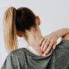 Women suffering with neck pain wearing a grey top against a white background