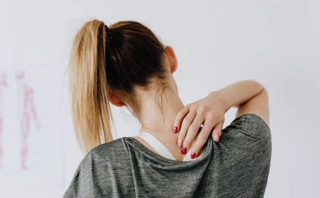 Women suffering with neck pain wearing a grey top against a white background