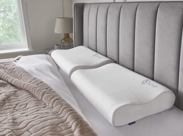 Slumbar Orthopaedic neck pillow being displayed on a grey bed with a brown throw